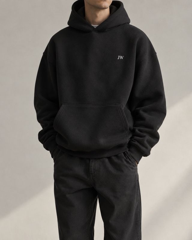 The black JW Hoodie worn with dark trousers, hands in the pockets.